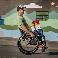 Middle aged man in a manual wheelchair rolling down a hill with items on his lap help in place with a lap stacker strap.