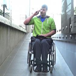 Man sitting on a manual wheelchair on the phone on a side walk.