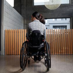 Back view of a young woman sitting in a manual wheelchair on a concrete floor.