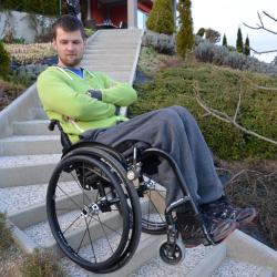 Man sitting in manual wheelchair with his arms crossed balancing on his two back wheels on stairs.