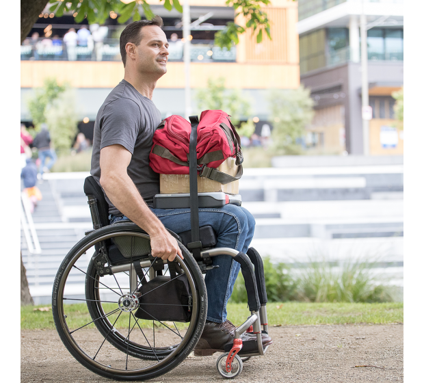 Side on view of man in a manual wheelchair with items stacked on his legs with the lap stacker strap holding the items in position.