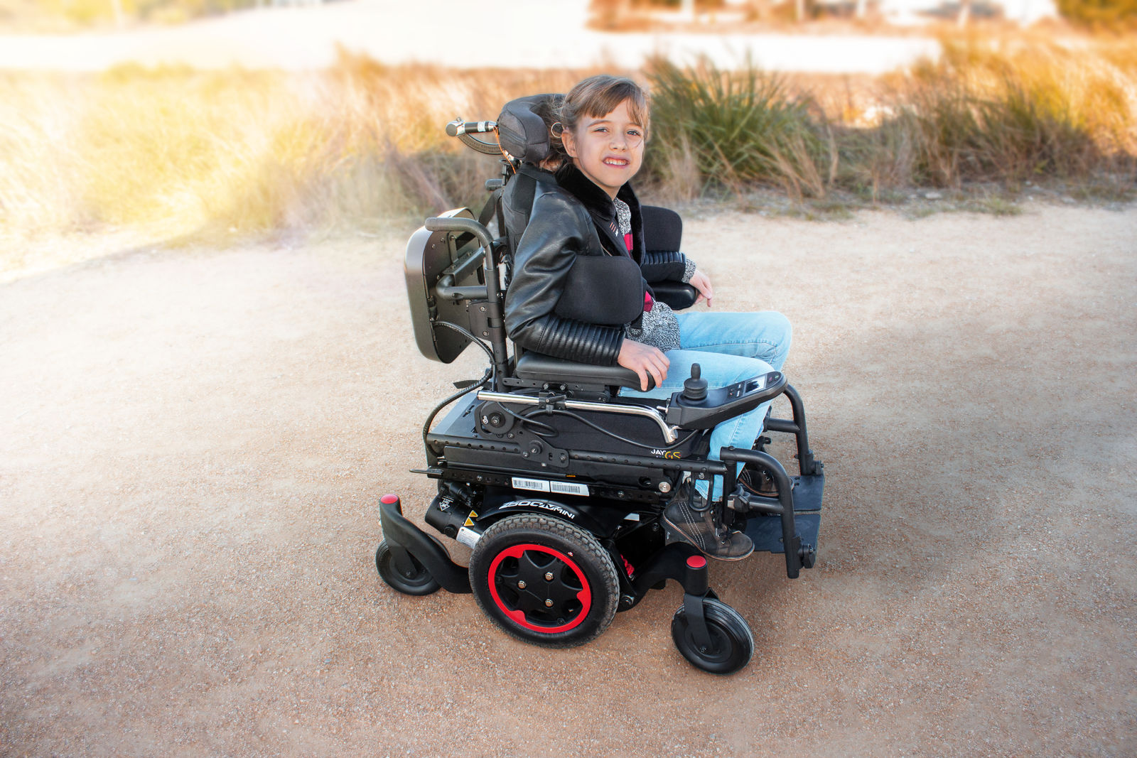 Young boy smiling while sitting in a Zippie Z300M powerchair on a concrete path.