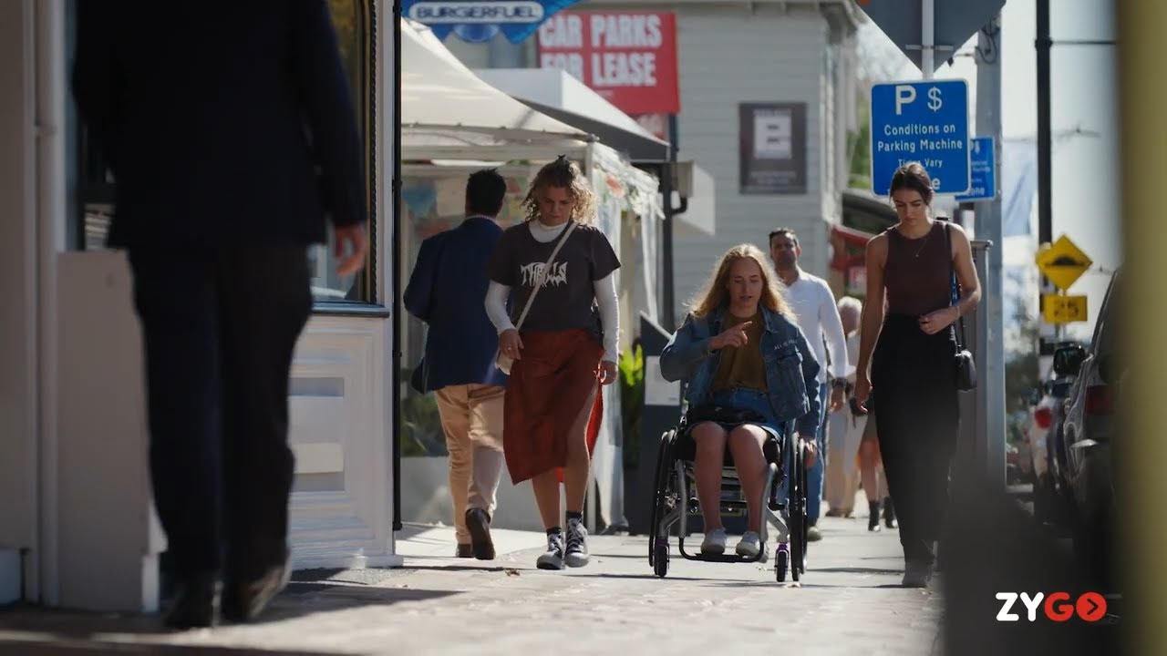 Pieta in her wheelchair with Zygo Active contour Lo back support, traveling down a city pavement, chattig with her freinds.