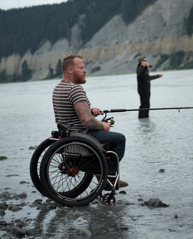 Curtis flying fishing with freinds from the edge of a river, in his manual wheelchair with a Zygo deep contour Lo back support.