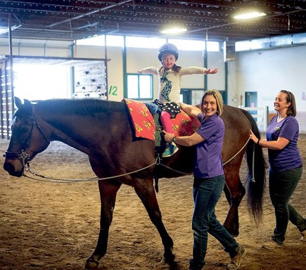 Little girl riding on horse with 2 helpers showing the saddle seat positioning