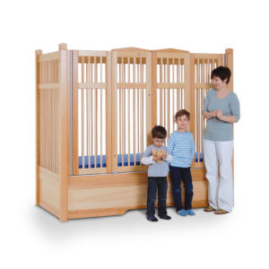 A mother and her two young sons stand by a Safe Surround Plus Bed with high timber sides and blue mattress for safety and stability.