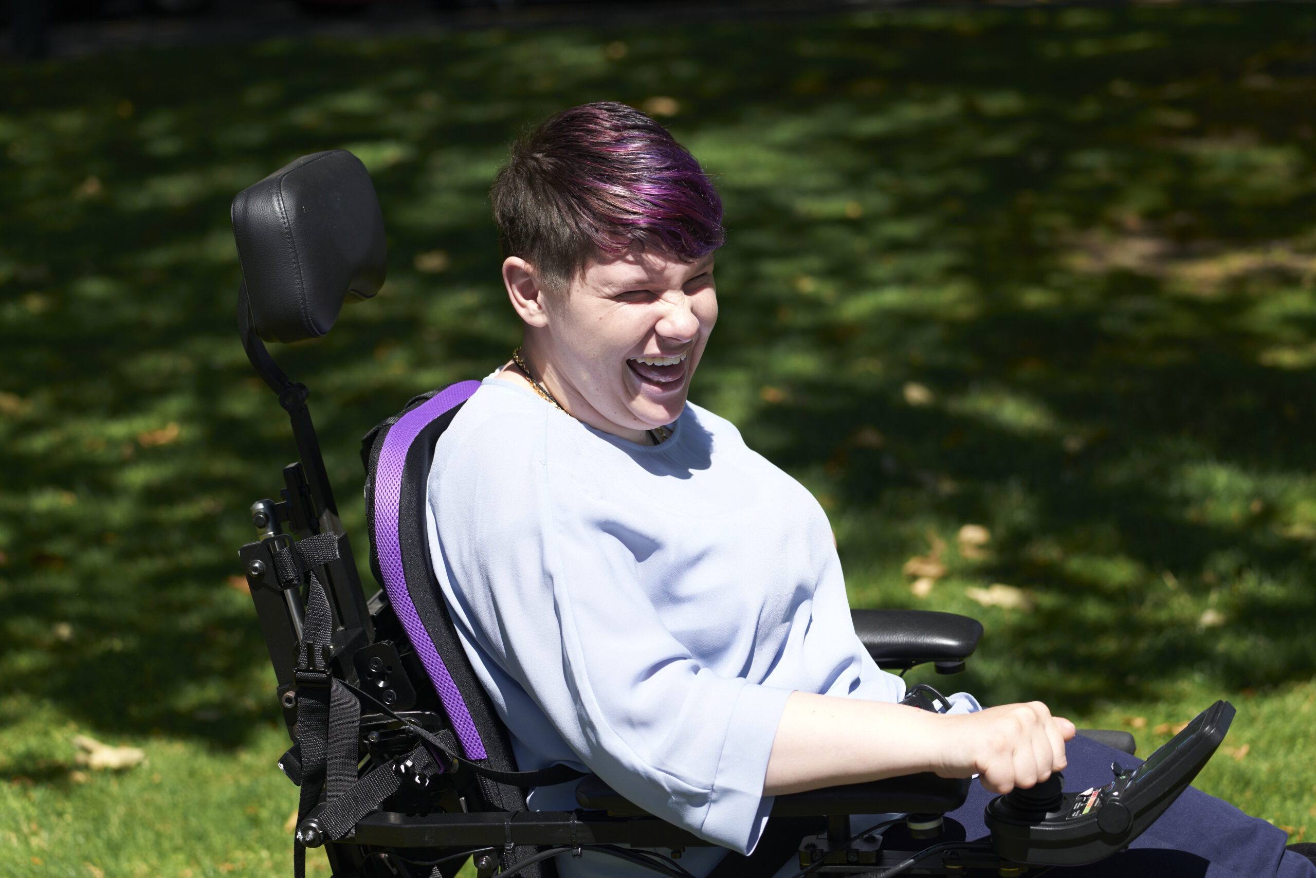 Nikayla smiling in the sun as she enjoys active daily life with purple Spex seating, benefiting from improved posture and mobility support.