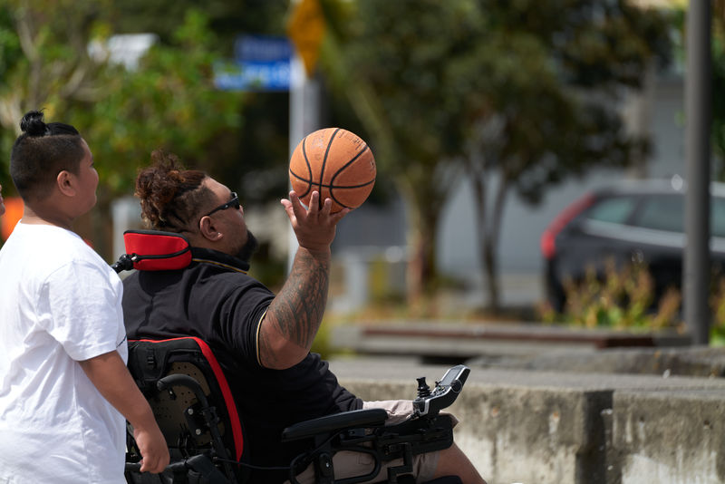 Taps sitting in his Spex XLella bariatric wheelchair seating while playing basket ball with his son.