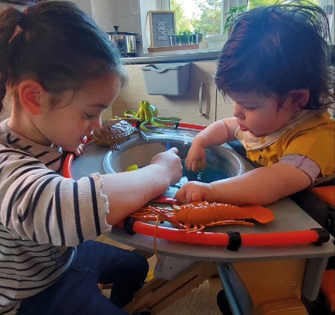 Young person smiling while engaging confidently with the table on the Jenx Standz with her sister, promoting independence and inclusion.