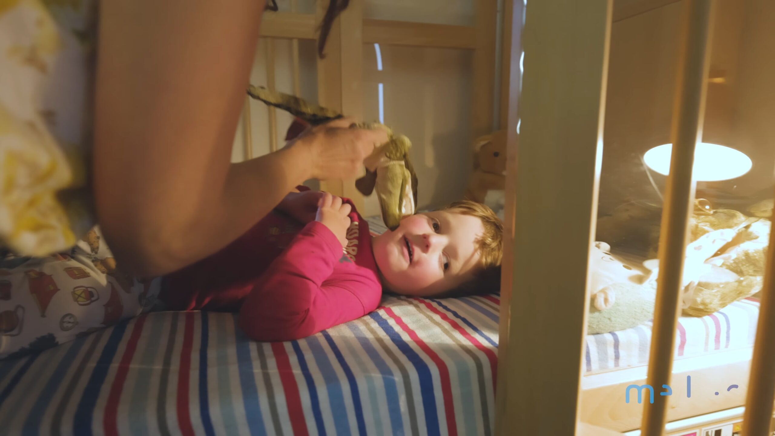 Close up image of small child in a Robbies Genie Bed with person holding dinosaur teddy near small child's face.