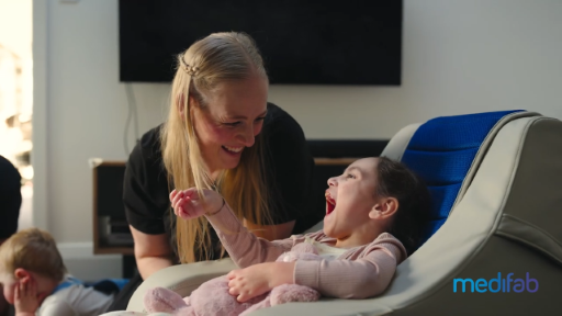 Little smiling Hazel enjoying postural support and comfort in her Gravity Chair at home as she interacts with her family.