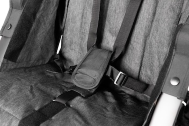 Close up image of 5-point harness against grey upholstery. The release button is covered with a black cover.