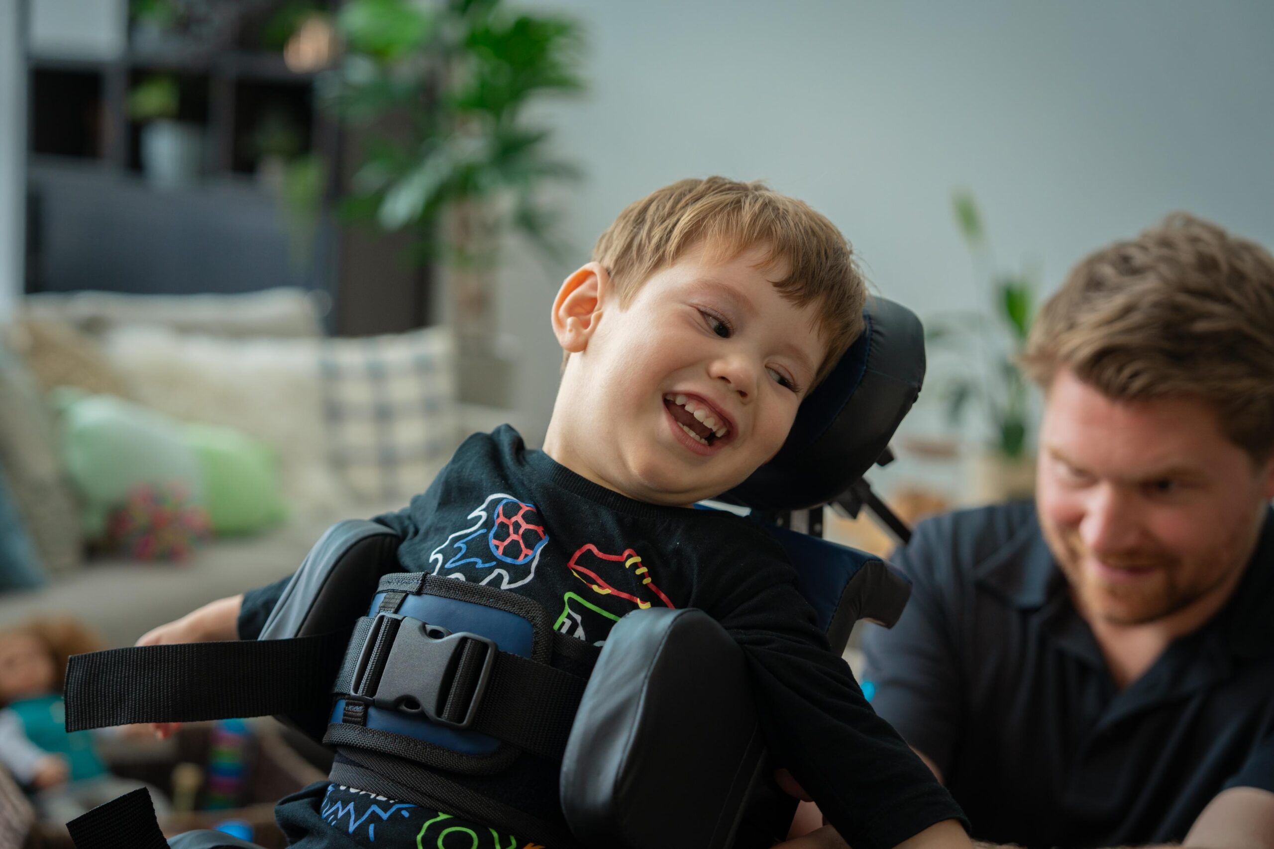 Close up profile of young boy smiling whilst standing in Ella Stander, whilst a rep re-adjusts the back support.